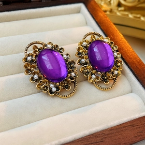Dettagli di orecchini vintage con gemma ovale viola, perle e base dorata in primo piano