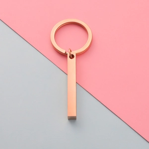 Detailed view of a rose gold bar keychain on a minimalist pink and grey background