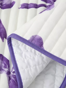 Close-up detail of white quilted fabric featuring purple floral patterns and piped edging