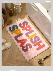 Plush pink bathroom mat with Splish Splash text on wooden floor next to bathtub