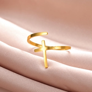 Close-up of golden cross adjustable ring on soft pink silk fabric with elegant lighting