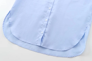 Détail d'une chemise en coton bleu clair avec ourlet courbé et fermeture à boutons blancs