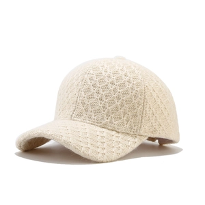 Close-up of beige knitted baseball cap showing intricate hollow knit texture and curved brim