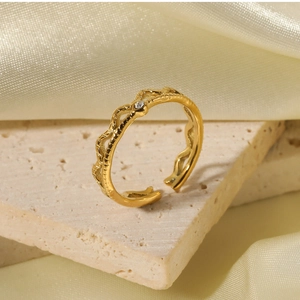 Detail of a wavy gold ring with a single clear zircon on a silk and stone backdrop