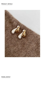 Detail of teardrop earrings with gold glossy and silver brushed finish on knit fabric