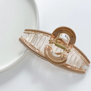 Close-up of transparent hair claw clip with caramel border and metal spring on white plate