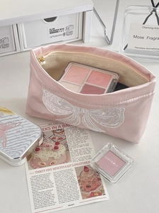 Pink satin cosmetic bag with white bow embroidery and pearl zipper pull on a desk