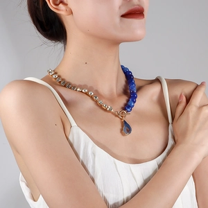Nahaufnahme einer asymmetrischen Halskette mit blauem Tropfenanhänger und Strass