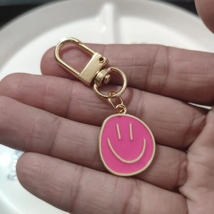 Close-up of pink enamel smiley face keychain with golden D-ring clasp and swivel