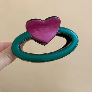 Gros plan d'une pince à cheveux ovale en acrylique vert avec un cœur rose brillant