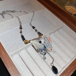 Macro detail of asymmetric butterfly pendant with Chinese calligraphy on beaded necklace