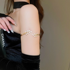 Detail of a gold-tone open upper arm cuff with white enamel leaf-shaped motifs on a black sleeve