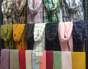 Multiple rows of colorful scarves with tassels in plaid and solid styles on a rack