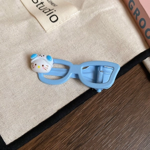 Detail view of a blue glasses-shaped hair clip with a cute 3D cartoon cat head