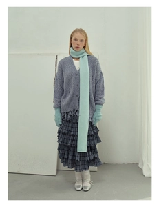 Close-up of blue wool knit scarf styled with matching cardigan and plaid skirt