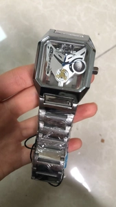 Macro detail of silver rectangular watch with skeleton dial showing gold gears and blue hands