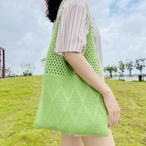 Green knit tote bag with geometric diamond hollow pattern shown in an outdoor park