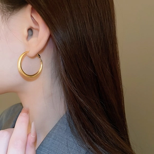 Detailed view of large gold hoop earrings with a brushed metal texture on a female model