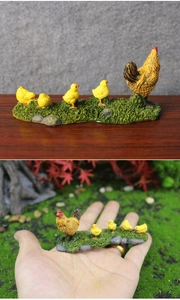 Miniature resin hen and chicks figurines on green grass base shown in hand for scale