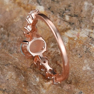 Detailed side view of rose gold oval blue stone ring on a textured rock base
