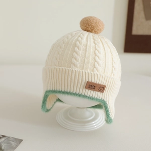 Close-up of cable knit baby hat featuring a cozy bear leather patch and pom-pom detail