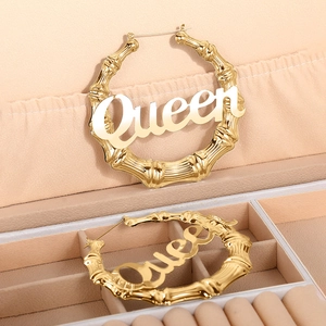 Detailaufnahme goldener Bambus-Creolen mit Queen-Schriftzug in einer Schmuckschatulle