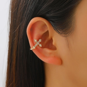 Macro view of gold-plated cross ear cuff with white zircons on a model's ear