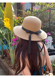 Detail of raffia straw sun hat featuring a wide brim and elegant black ribbon bow tie