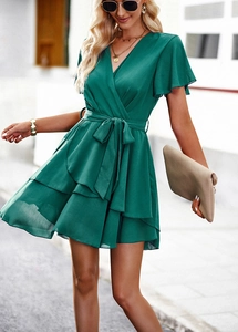 Détail d'une robe verte à col en V avec taille nouée et ourlet à volants superposés