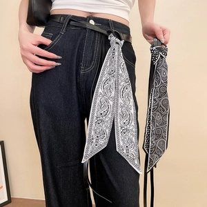Détail d'un foulard en soie à motif paisley attaché à une fine ceinture en cuir noir