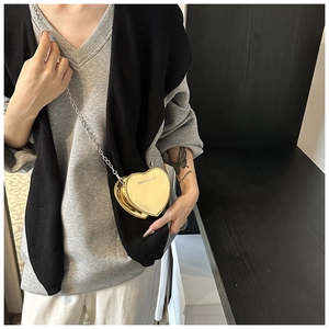 Detail of a mini gold heart-shaped crossbody bag with a silver chain strap and text
