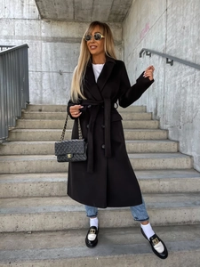 Street style view of a black mid-length wool coat with belted waist and buttoned cuffs