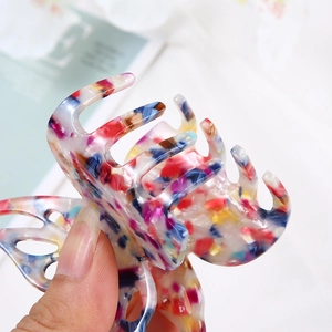 Close-up of a hand holding a butterfly hair clip with colorful abstract resin patterns