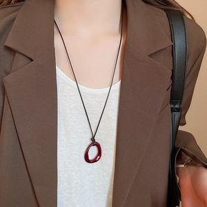 Gros plan d'un pendentif géométrique en résine rouge foncé sur un collier en cordon noir