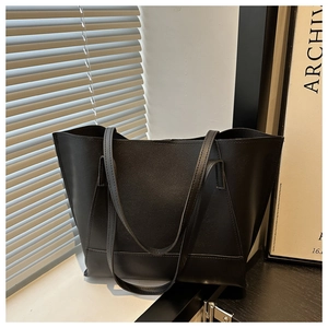 Close-up of a large black leather tote bag showing a refined matte texture in natural light