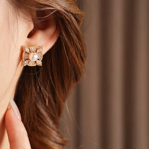 Close-up of elegant gold square pearl earring with zircon halo worn by a model