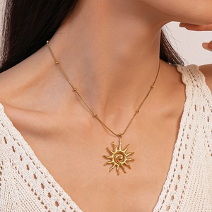Detail of gold sun pendant necklace with spiral design worn on neck by a model