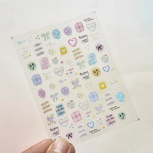 Close-up of macaron color nail stickers featuring hearts, bows, and cute English phrases