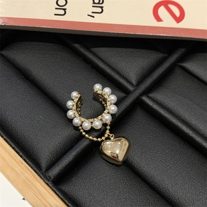 Dettaglio dell'ear cuff placcato oro con perle bianche e ciondolo a cuore con nappina