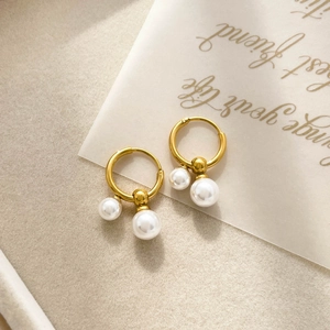 Detail of gold circular earrings with double white pearl drops on beige felt surface