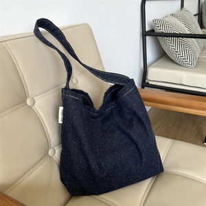 Dettaglio della borsa tote in denim blu scuro con etichetta su una sedia in pelle bianca