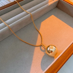 Close-up of golden stainless steel ball pendant necklace on a velvet jewelry tray