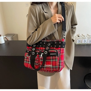 Detail of red tartan tote bag with punk rivet straps and functional front zipper pockets