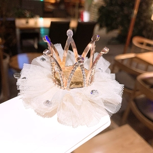 Detailed close-up of a golden crown hair clip with rhinestones and white tulle base