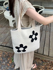 Detail of a beige knitted tote bag featuring black floral patterns in a casual outdoor setting