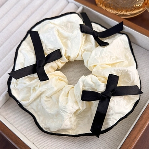 Detail of cream pleated scrunchie with black lace trim and ribbon bows in a wooden tray
