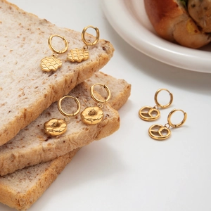 Detailed close-up of gold food-themed hoop earrings set on rustic bread slices