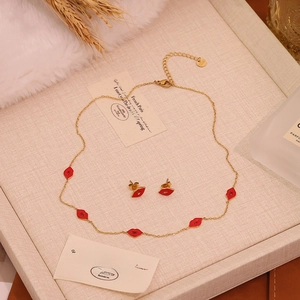 Detail of gold necklace set featuring red lip enamel pendants on woven background