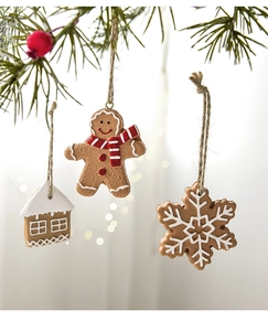 Close-up of resin gingerbread man, snow house and snowflake hanging on a pine branch