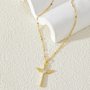 Golden cross necklace with wings and heart stone on white textured background